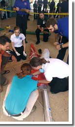 Paramedic student Dylan Rodgers (blue shirt on left) is keeping a close eye on a HOSA EMT team. SFC student Jacob Exley (with hat) plays an older person having trouble breathing while another SFC student actor (Ryan Griffith) is being placed on a long spine board by the HOSA EMT team.