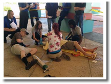 Paramedic student Drew Little (right side) & EMT student Greg Sanford (on one knee) looks on as a HOSA EMT team treats an injured patient. SFC Student Edwin Vickers (left) plays a concerned father to the injured patient being treated.