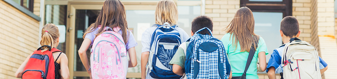Elementary school kids with backpacks walking to school entrance